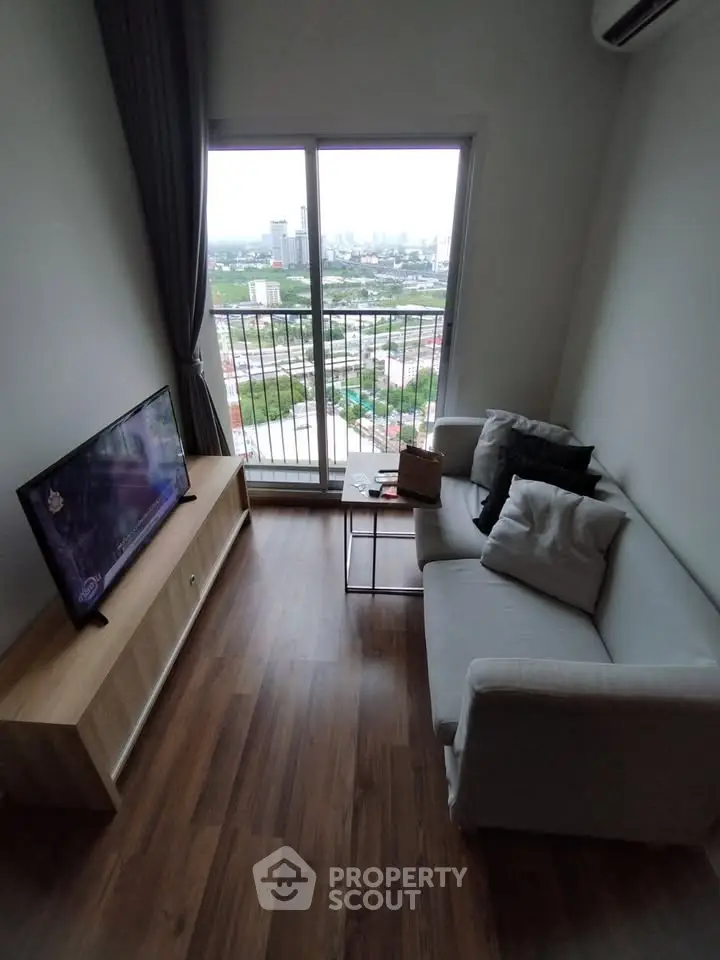Cozy living room with city view from balcony, featuring modern furniture and wooden flooring.