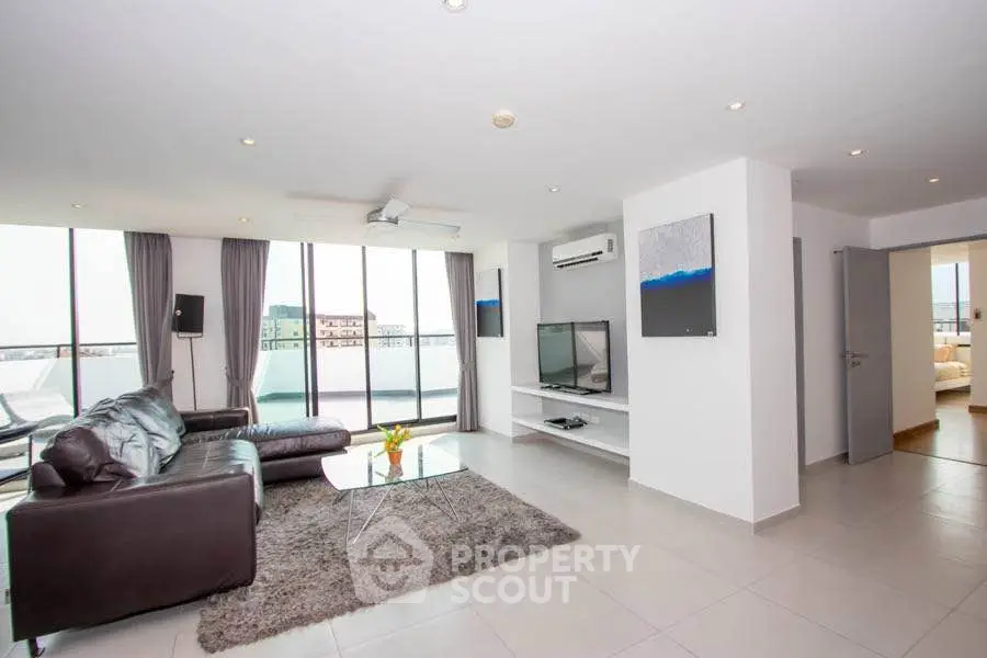 Spacious modern living room with leather sofa and large windows offering city views.