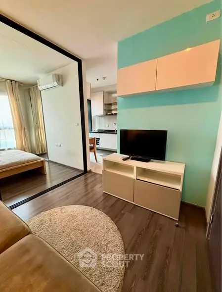 Modern living room with TV, open layout to bedroom and kitchen, stylish decor.