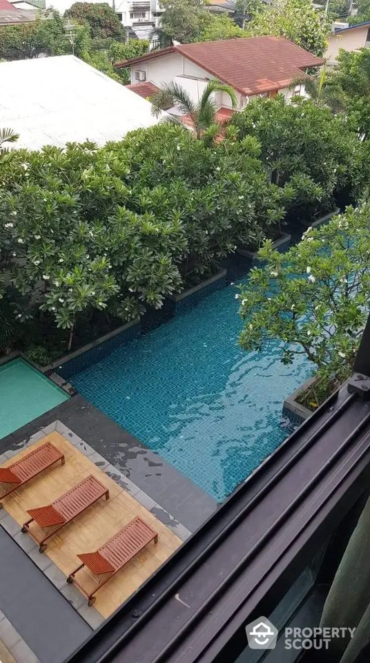 Luxurious residential pool view with lush greenery and sun loungers, perfect for relaxation.