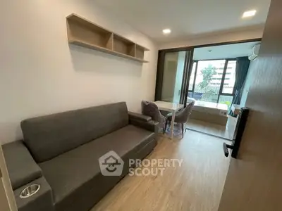 Modern living room with sleek sofa and dining area, featuring large windows and natural light.