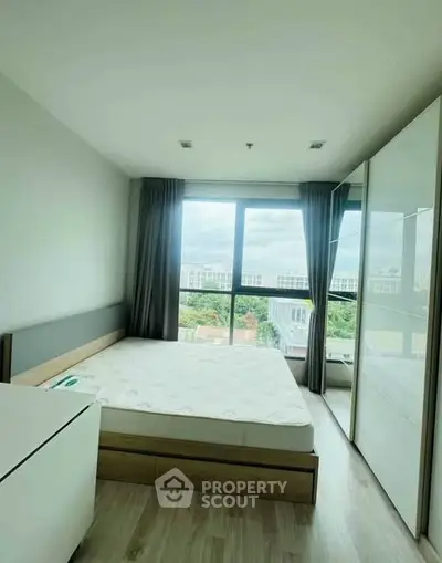 Bright bedroom with large window and modern furnishings in a high-rise apartment.