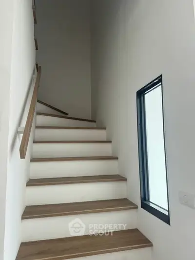 Modern staircase with wooden steps and sleek handrail in a minimalist home interior.