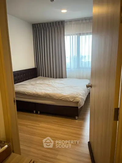 Cozy bedroom with wooden flooring and large window, perfect for relaxation.