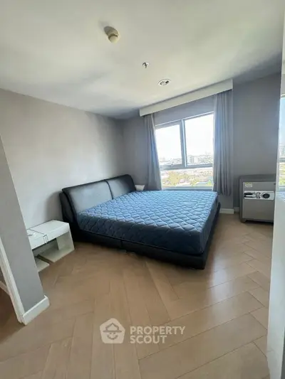 Spacious bedroom with large window and modern furnishings in a high-rise apartment.