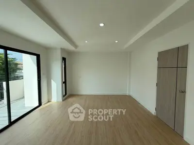 Spacious empty room with wooden flooring and large windows leading to a balcony, perfect for customization.