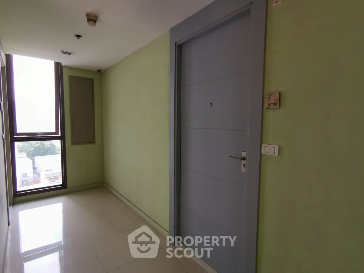 Modern apartment hallway with sleek door and large window view.