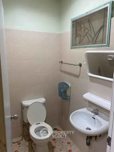 Compact bathroom with toilet, sink, and wall-mounted mirror in a tiled setting.