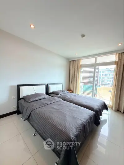 Spacious bedroom with twin beds and large window offering city views in modern apartment.