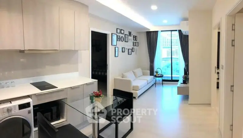 Modern open-layout living room with kitchen and dining area, featuring sleek furniture and large windows.