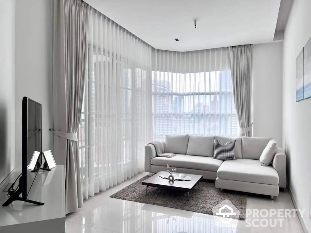 Spacious and modern living room with abundant natural light, featuring a large L-shaped sofa, sleek flat-screen TV, and elegant sheer curtains.