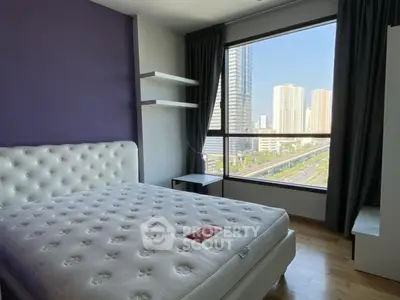 Modern bedroom with large window offering stunning city view in high-rise apartment.