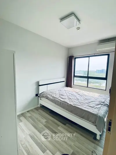 Bright bedroom with large window and modern furnishings, offering a serene view.