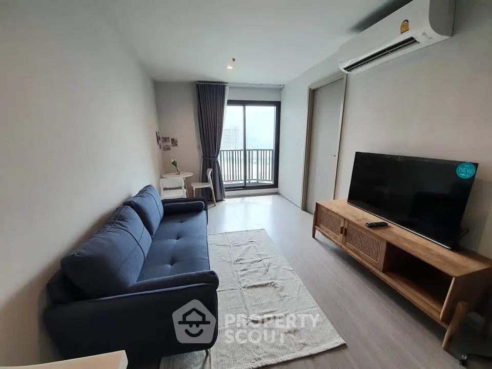 Modern living room with balcony view, featuring a blue sofa, TV, and air conditioning.