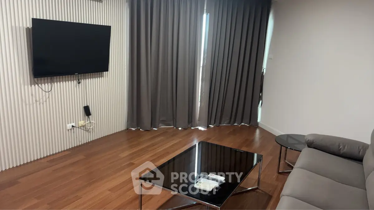 Modern living room with sleek furniture and wall-mounted TV, featuring elegant wooden flooring and stylish curtains.