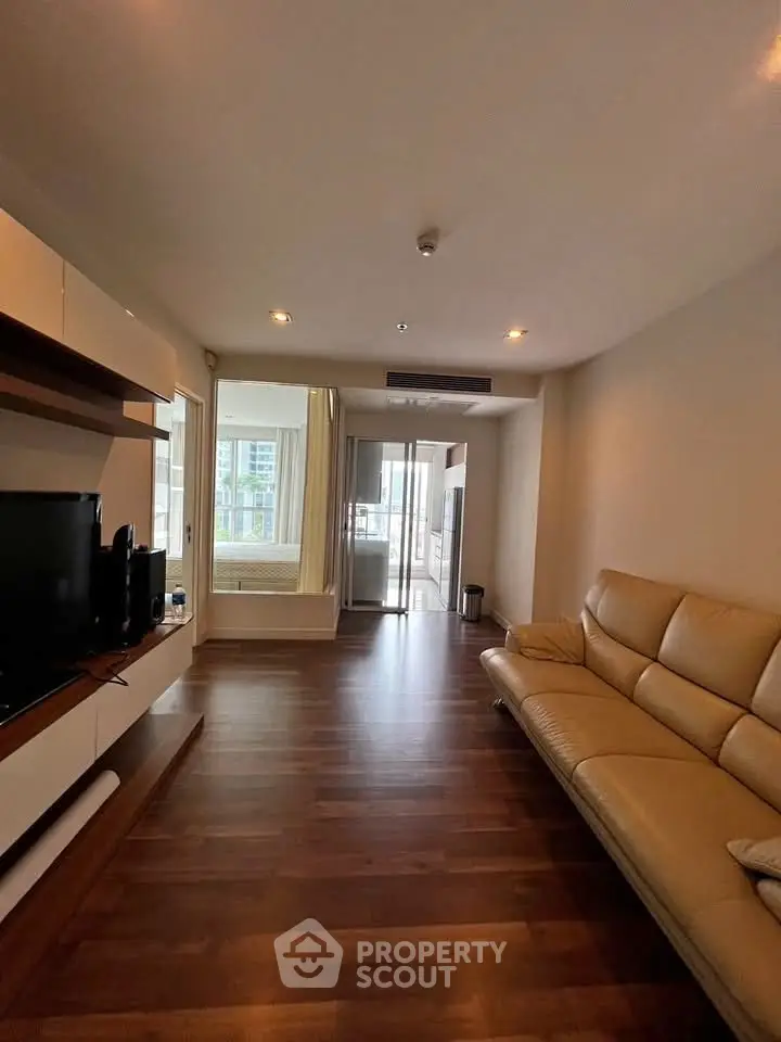 Spacious living room with modern leather sofa and wooden flooring, featuring a bright window view.