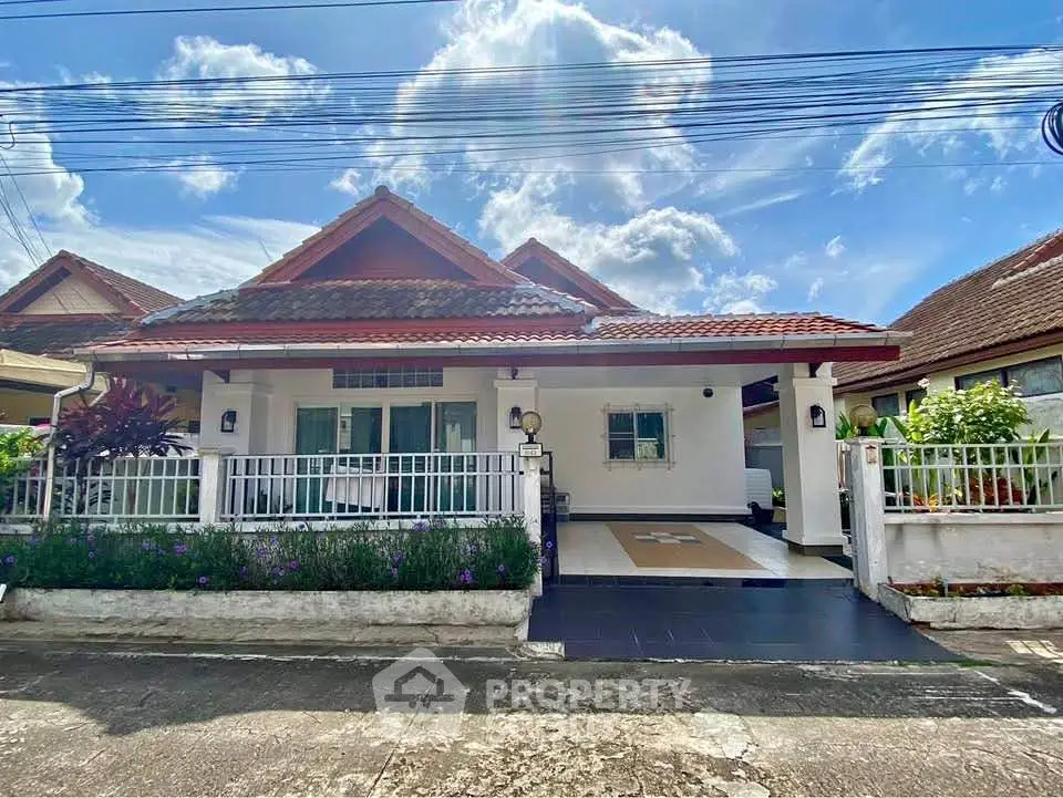 Charming single-story house with tiled roof and gated driveway under a bright blue sky.