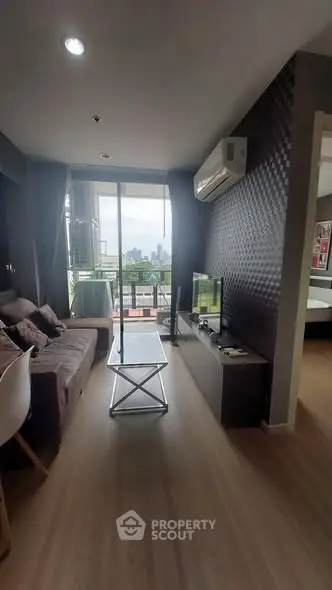 Modern living room with balcony and city view, featuring sleek furniture and natural light.