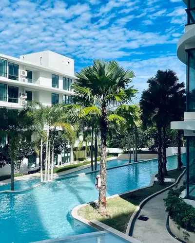 Luxurious apartment complex with stunning pool and lush palm trees under a vibrant blue sky.