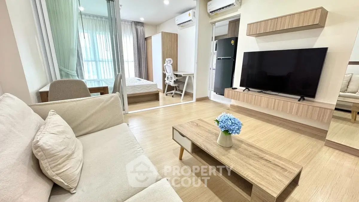 Modern living room with sleek furniture and large TV, adjacent to a cozy bedroom.