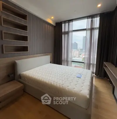 Modern bedroom with large window and city view, featuring a stylish bed and wooden flooring.