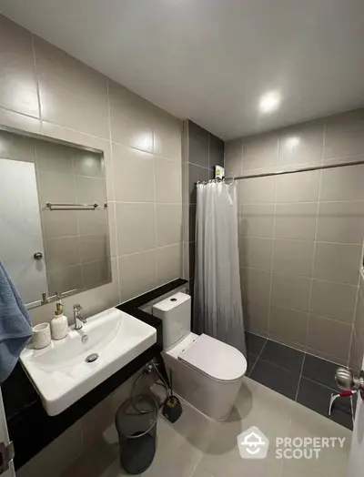 Modern bathroom with sleek fixtures and neutral tiles, featuring a shower and stylish sink area.