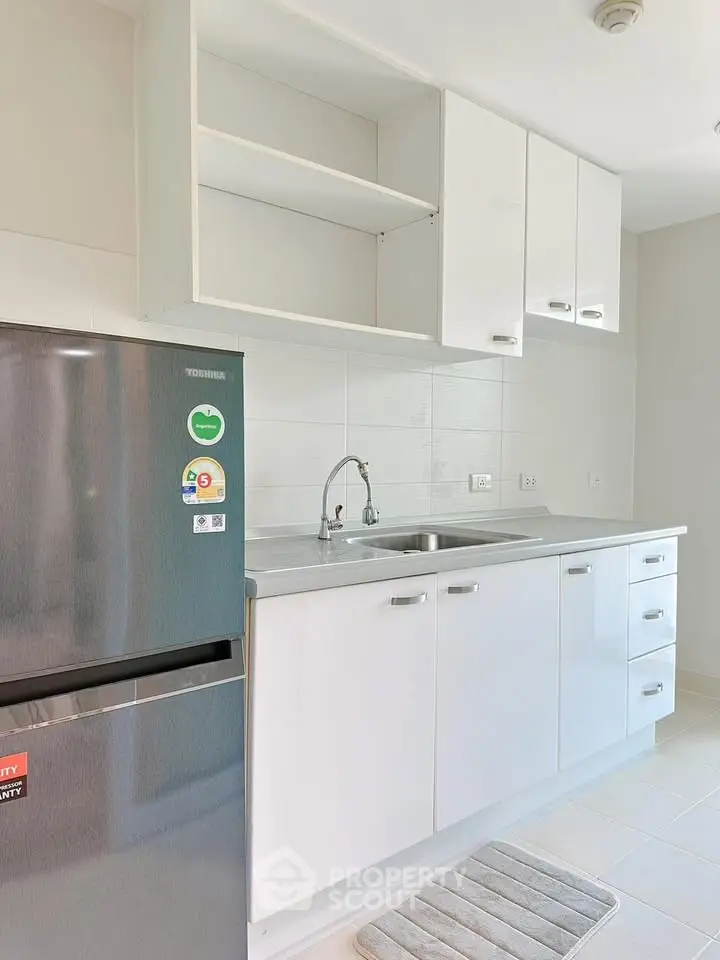 Modern kitchen with sleek white cabinets and stainless steel fridge in a bright apartment.