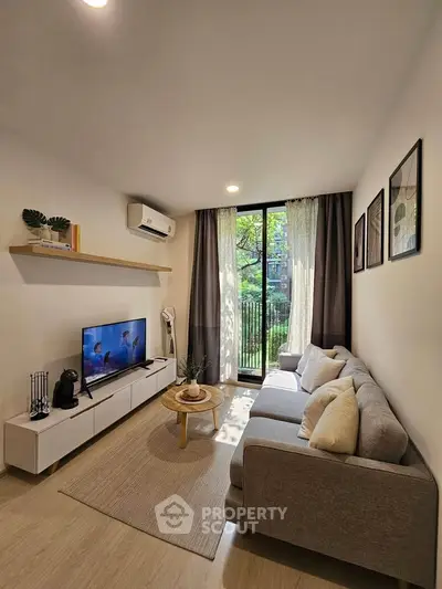 Modern living room with cozy sofa, wall-mounted TV, and large window overlooking greenery.
