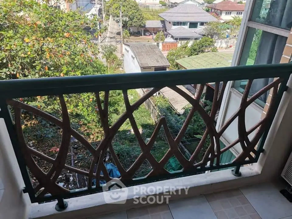 Charming balcony with artistic railing offering a lush green view in a serene neighborhood.