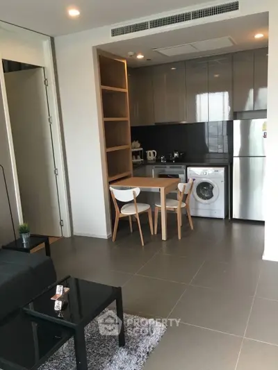 Modern kitchen with sleek cabinetry, dining area, and in-unit washing machine in stylish apartment.