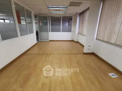 Spacious office space with wooden flooring and large windows for natural light.