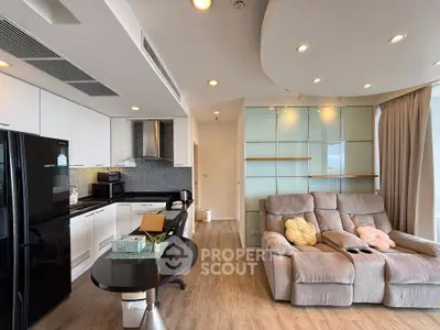 Modern open-layout living room with sleek kitchen and cozy seating area, featuring large windows and stylish decor.