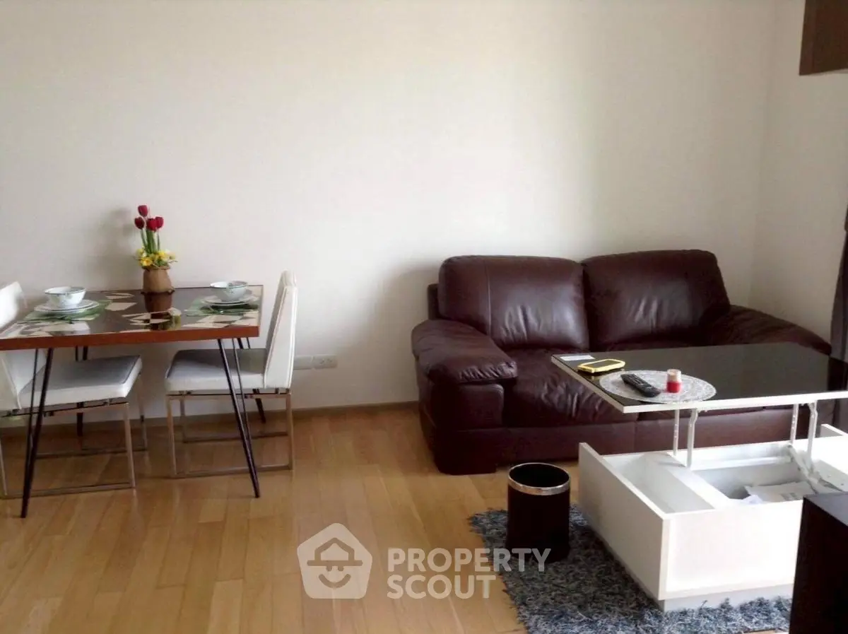 Cozy living room with leather sofa and dining area on wooden flooring.