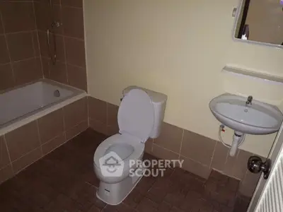 Modern bathroom with bathtub, toilet, and sink in a tiled setting.