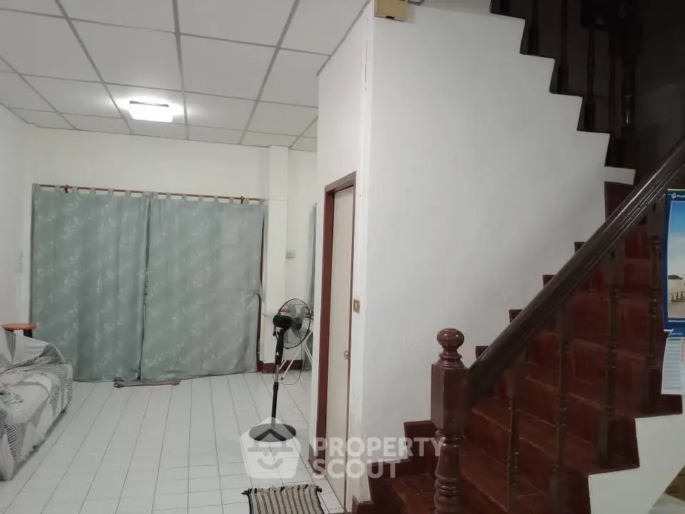 Spacious living area with tiled floor and wooden staircase, ideal for family gatherings.