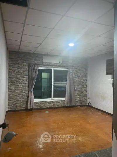 Spacious empty room with parquet flooring and stone accent wall, ideal for customization.