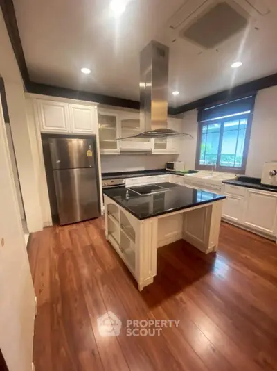 Spacious kitchen with modern island and wooden flooring, featuring stainless steel appliances.