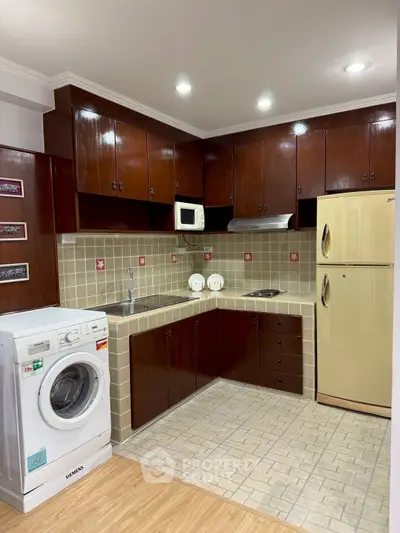 Charming kitchen with wooden cabinets, washing machine, and fridge, perfect for modern living.