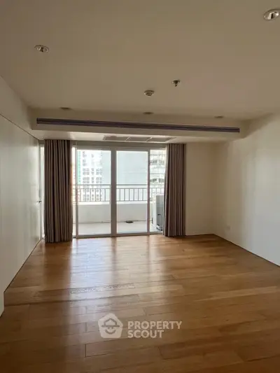 Spacious living room with wooden flooring and balcony access in modern apartment.