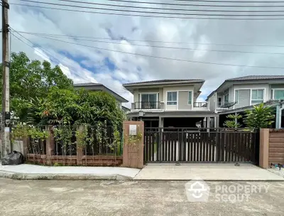 Modern two-story house with gated entrance and lush greenery in suburban neighborhood.