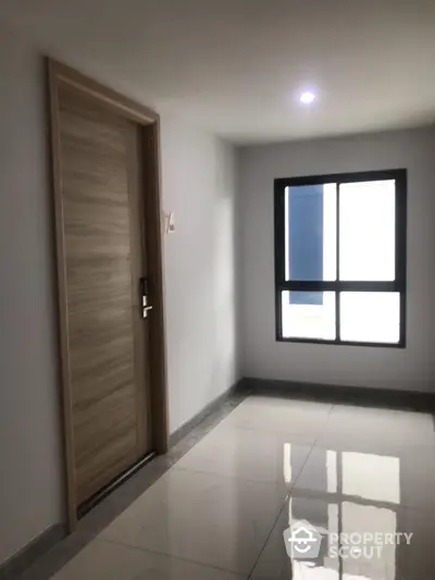 Modern apartment hallway with sleek wooden door and large window.