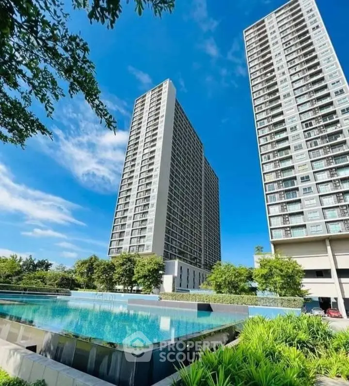 Luxurious high-rise condos with stunning pool and lush greenery under clear blue sky.