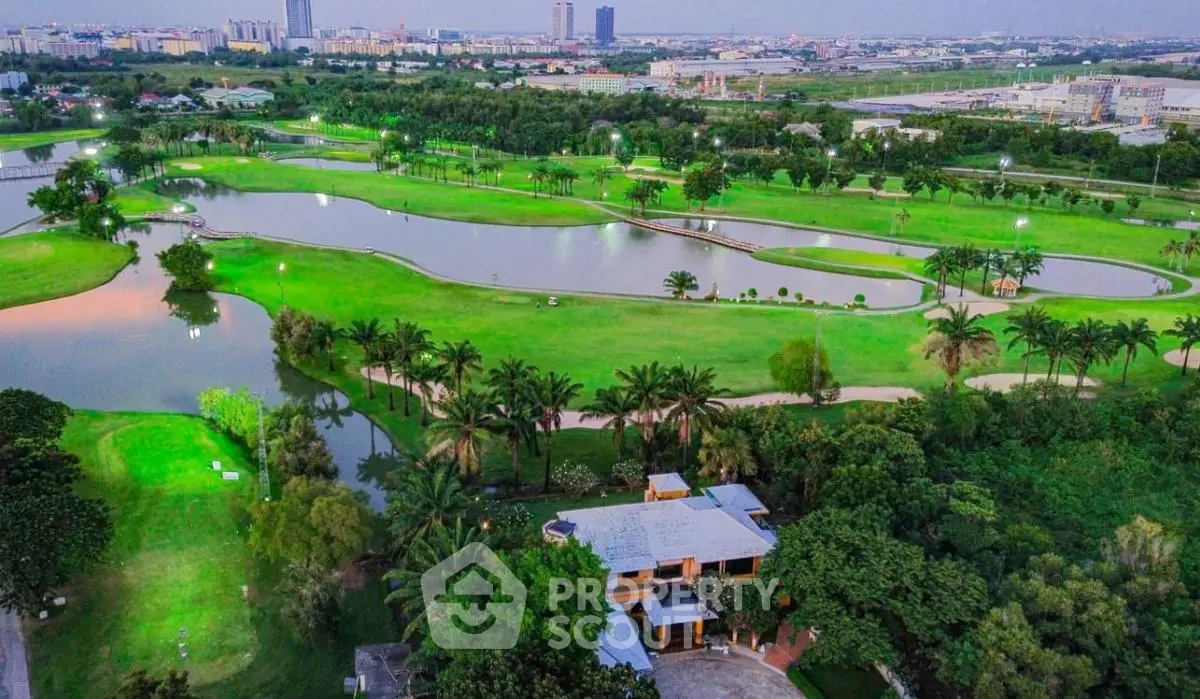 Stunning aerial view of lush green golf course with serene water features and modern cityscape backdrop.