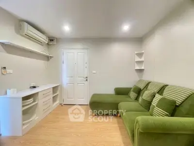 Modern living room with green sofa and minimalist decor, featuring wooden flooring and air conditioning.