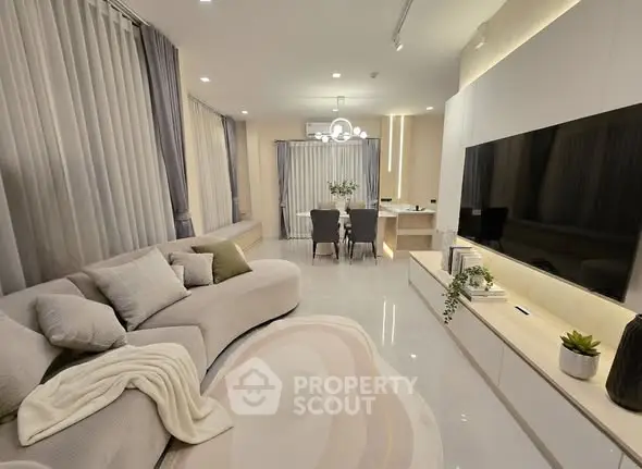 Elegant modern living room with stylish decor and open dining area, featuring a large TV and cozy seating.