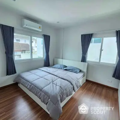 Modern bedroom with wooden flooring and large windows in a bright apartment