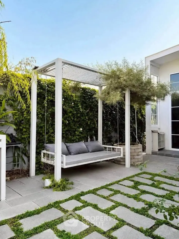 Charming outdoor patio with modern swing and lush greenery, perfect for relaxation and entertaining.