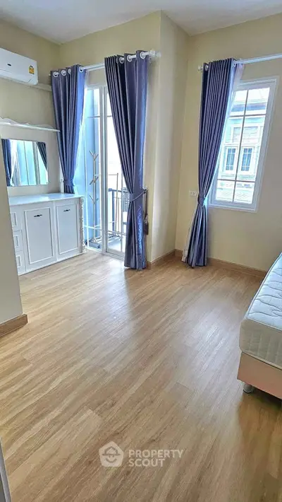 Bright bedroom with wooden flooring and balcony access, featuring elegant curtains and ample natural light.