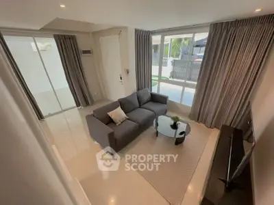 Modern living room with sleek gray sofa, large windows, and stylish decor in a contemporary home.