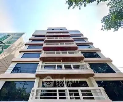 Modern multi-story building with large windows and balconies in urban setting.